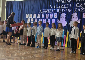 Pani Dyrektor pasuje wielkim ołówkiem uczniów klas pierwszych.