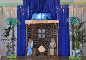 Uczniowie grający Maryję i Józefa siedzą w szopce betlejemskiej.