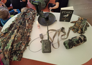 Sprzęt fotograficzny - fotopułapka, strój maskujący, książka o ptakach.