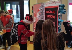 Uczniowie na szkolnym korytarzu przy plakacie mikołajkowym.