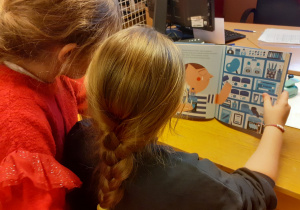 Dwie dziewczynki z klasy 1 czytają i przeglądają książkę z serii Mali Wielcy.